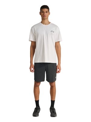 Homme debout portant une chemise blanche à manches courtes avec un petit texte, un short cargo noir, des chaussettes noires et des chaussures de sport noires, faisant face à l'avant.