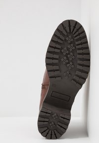 Botte en cuir marron avec une semelle noire en caoutchouc robuste. Présente des crampons profonds et une tige lisse avec des détails discrets de couture. Taille 37.