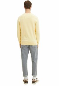 Light yellow knit sweater, gray relaxed-fit jeans, and white sneaker with brown and navy accents. Simple design, no visible patterns.