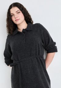 Dark gray knitted dress with a collared neckline, button detail, rolled sleeves, and a tied waist for a relaxed fit. Soft texture.