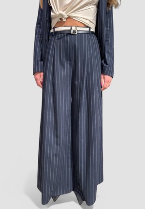 Pantaloni a gamba larga a righe navy realizzati in tessuto morbido, con vita alta e una cintura abbinata con una fibbia in argento. I pantaloni presentano delle pieghe.