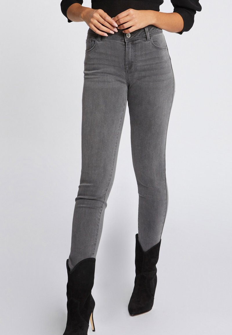 Jeans skinny grigi con un design a vita alta, caratterizzati da una leggera sfumatura e tasche frontali. Abbinati a stivaletti neri in suede con tacco.