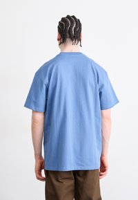 Lichtblauwe katoenen T-shirt met een relaxte fit, korte mouwen en een ronde hals, gedragen met bruine broek. Minimalistisch ontwerp, geen zichtbare logo's.