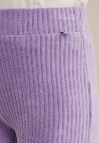 Pantaloni din corduroy mov cu nervuri, având o textură moale, talie largă și dungi verticale, cu un detaliu de buzunar pe spate vizibil.