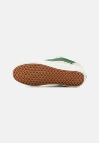 Shoe sole featuring a brown rubber base with a lattice pattern, cream sidewalls, and green leather accents on a beige upper.