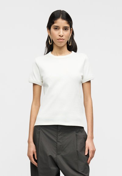 T-shirt blanc à manches courtes avec un col rond et des manches retroussées, en tissu doux. Porté avec un pantalon sombre taille haute.