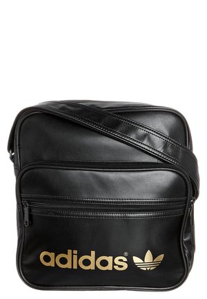 Sac bandoulière Adidas noir avec logo doré, poche zippée à l'avant et sangle d'épaule ajustable sur fond blanc.