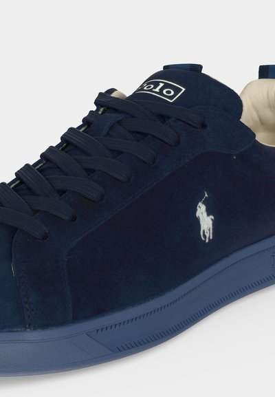 Ναυτικό μπλε σουέντ αθλητικό παπούτσι με σκούρα κορδόνια, λευκό λογότυπο παίκτη πόλο στο πλάι και επενδεδυμένη μπεζ εσωτερική επένδυση.