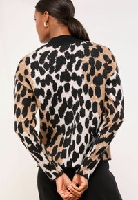 Kootud sviiter, millel on leopardimuster mustas, pruunis ja valges. Sobivad varrukate ja äärisega koos ümarate kaelustega. Pehme tekstuur.