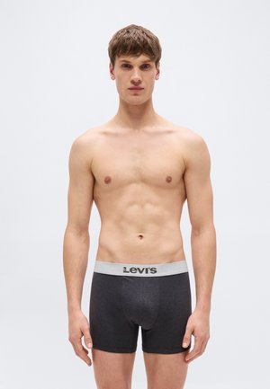 Νεαρός άνδρας όρθιος, χωρίς πουκάμισο, φοράει σκούρα γκρι εσώρουχα boxer της Levi's με ανοιχτό γκρι ζώνη μέσης, σε απλό λευκό φόντο.