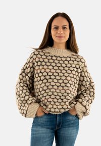 Maglione lavorato a maglia color crema con motivo geometrico multicolore, caratterizzato da un ampio colletto e polsini a coste. Abbinato a jeans denim blu.