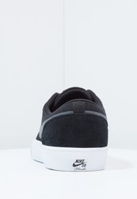 Mustat lenkkarit, joissa on mokka- ja verkkopäällinen, valkoinen kumipohja ja hopeinen yksityiskohta. Varressa on Nike SB -logo.