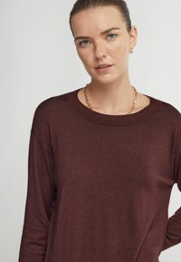 Burgundy stickad tröja med rund halsringning och långa ärmar. Slät textur, avslappnad passform och ribbade muddar ger subtila detaljer.