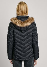 Zwarte pufferjas met een chevron-quiltpatroon, nepbontafwerking op de capuchon en aansluitende mouwen. Heeft een taille die cinched is voor een mooie vorm.