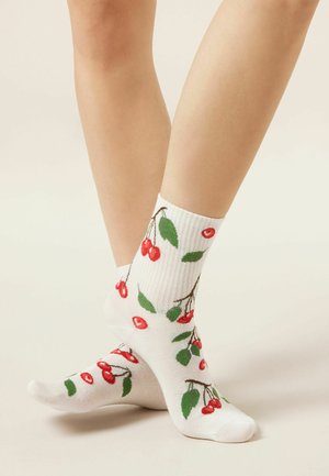Benen met witte enkelsokken versierd met rode kersen en groene bladeren op een neutrale achtergrond.