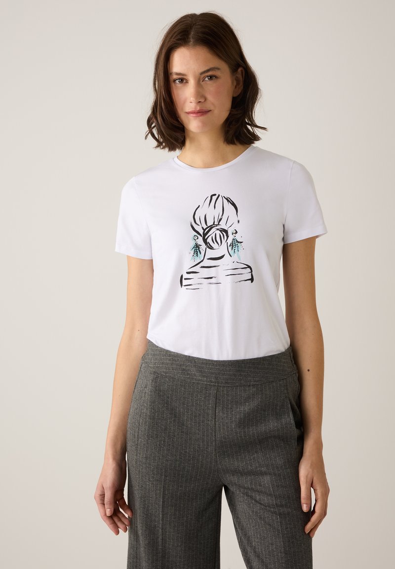 White cotton t-shirt featuring a black line drawing of a hairstyle with turquoise accents. Worn with gray pinstriped trousers.