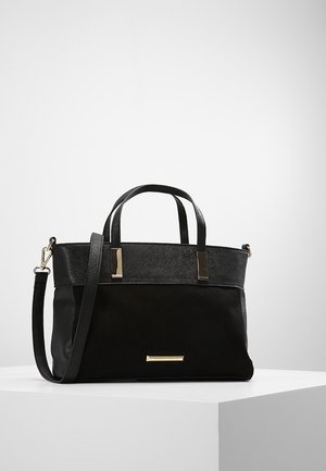 Borsa nera con due manici corti, una tracolla regolabile e dettagli in metallo dorato rettangolari, posata su una superficie bianca.