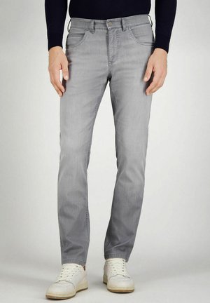 Mann trägt hellgraue Slim-Fit-Jeans und weiße Sneakers, steht vor einem einfarbigen Hintergrund.