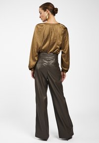 Bruine blouse met textuur en luchtige mouwen, gecombineerd met high-waisted donkergroene leren broek. Heeft een aangesloten tailleband en achterzakken.