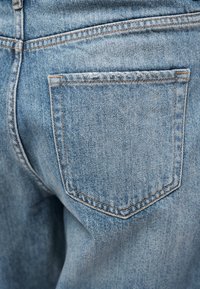 Κοντινό πλάνο σε τζιν παντελόνι ανοιχτού μπλε χρώματος που δείχνει την πίσω τσέπη και τις λεπτομέρειες της ραφής.