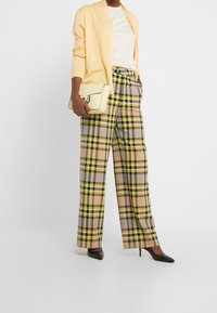 Cardigan giallo, t-shirt bianca, pantaloni a quadri gialli, grigi e neri, e décolleté nere a punta; tiene in mano una borsa crema con pattina.