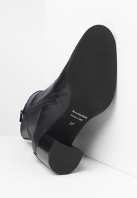 Stivale alla caviglia in pelle nera con punta rotonda, zip laterale e suola in gomma texture. Presenta un tacco a blocco e dettagli del marchio stampati.