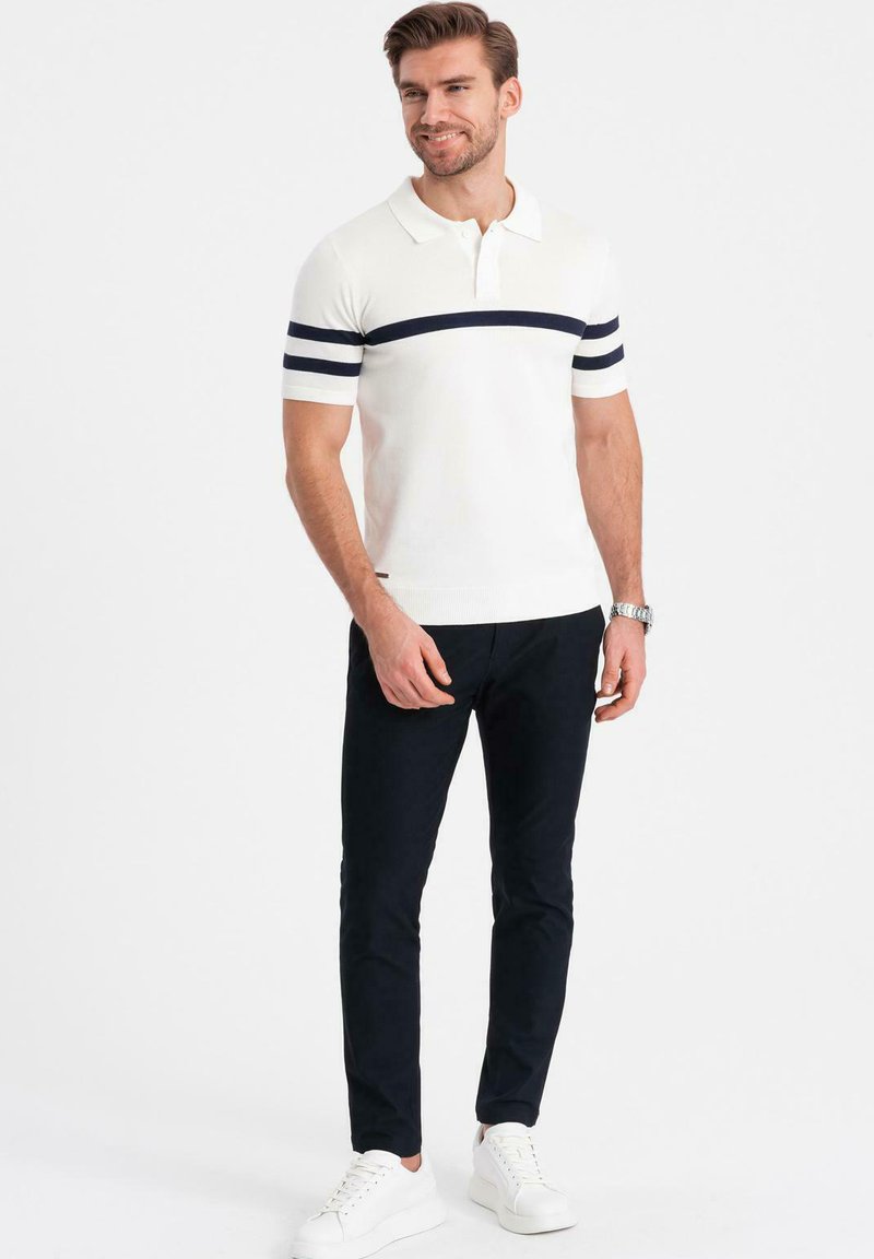 Vit pikétröja med marinblå horisontella ränder, korta ärmar. Kombinerad med mörka byxor och vita sneakers. Enkel design, lättviktigt material.