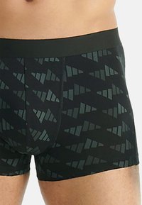 Svarta boxershorts med ett mörkt geometriskt triangelmönster, bärs av en person som visar midja och övre lår.