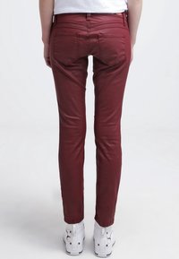 Vinröda smala byxor med slät yta, fem fickor och en åtsittande design, i kombination med vita högskor.