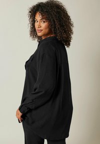 Czarna, długosleeve koszula z teksturowej tkaniny, z kołnierzykiem zapinanym na guziki, pojedynczą kieszenią na piersi oraz luźnym krojem.