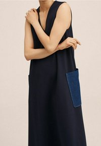 Vestido sin mangas azul marino con un escote en V profundo, que presenta un único bolsillo de mezclilla azul en el frente. Textura de tela suave con un corte holgado.