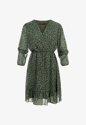 Zielona sukienka do kolan z nieregularnymi czarnymi plamami, dekoltem w serek, talią podkreśloną paskiem, długimi przezroczystymi rękawami i falbaną na dole.