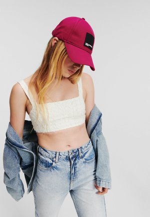 Il cappello è realizzato in tessuto fucsia con una toppa nera. Indossato con un crop top bianco testurizzato e jeans a vita alta blu chiaro, sovrapposto a un giubbotto di jeans.