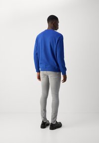 Sudadera azul de manga larga, cuello redondo y puños acanalados; combinada con jeans ajustados gris claro y zapatos negros.
