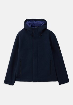Giacca con cappuccio blu navy realizzata in tessuto testurizzato, dotata di una tasca sul petto con zip e due tasche laterali con zip, con un rivestimento viola a contrasto.