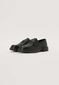 Črne loafer čevlje iz teksturirane usnje z elegantnim dizajnom. Imajo nizek blok peto in trak čez nart z kovinskim poudarkom.