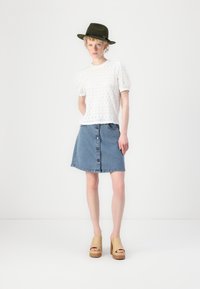 Witte kanten top met pofmouwen, gecombineerd met een lichtblauw denim A-lijn rok met knopen aan de voorkant, en tan platform sandalen met houten hakken.