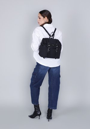 Zaino in nylon nero con texture morbida, tasche frontali duali, spallacci regolabili e design moderno, indossato sulla schiena di una figura.