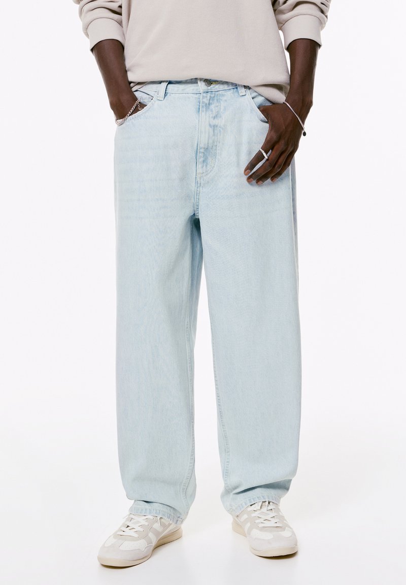 Lichtblauwe, losvallende denim jeans met een ontspannen ontwerp, met een rechte pijp, riemlussen en subtiele vervaging. Een paar witte sneakers eronder.
