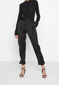 Pantalon cargo noir taille haute avec ceinture, doté de grandes poches, jambes fuselées et poignets réglables à boucle. Haut à manches longues noir.