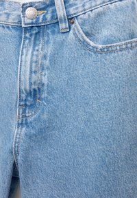 Jean en denim bleu clair avec bouton métallique, poche avant, passants pour ceinture et surpiqûres orange visibles.