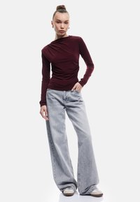 Bordeaux lange mouwen top met rimpeling, gecombineerd met lichtgrijze wijde jeans en beige sneakers. Soepele stof met een slim fit.