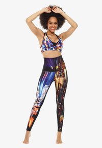Bunte Sport-BH und hochgeschnittene Leggings mit Drucken von urbanen Nachtlandschaften. Hergestellt aus dehnbarem, atmungsaktivem Material mit einer glatten Textur.