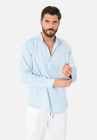Camicia a maniche lunghe azzurro chiaro con colletto a bottoni, caratterizzata da una vestibilità morbida e una texture soffice. Dettaglio notevole: polsini delle maniche con bottoni.