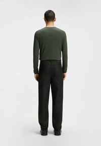 Dark green long-sleeve shirt with a fitted design, paired with straight-cut black jeans. Black shoes complete the outfit.