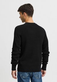Pulover negru cu reiat, cu mâneci lungi și guler rotund, având un finisaj texturat și manșete ajustate, asortat cu blugi din denim.