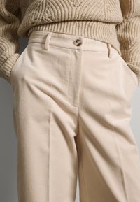 Beige Cordhosen mit hoher Taille, seitlichen Taschen, einem Knopfverschluss und vertikaler Rippstruktur.