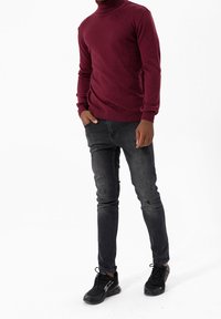 Suéter de cuello alto burdeos, diseño ajustado, combinado con pantalones vaqueros negros desgastados y zapatos deportivos negros. Textura suave, estilo casual.