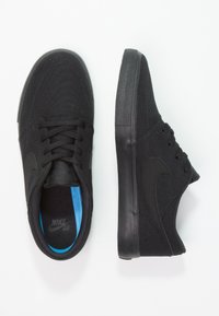 Baskets noires avec une tige en toile, semelle plate en caoutchouc noir et marquage ton sur ton. Dotées d'une semelle intérieure bleue et d'un système de laçage standard.