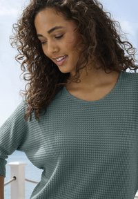 Türkisfarbener strukturierter Pullover mit Rundhalsausschnitt und Dreiviertelärmeln, der ein geripptes Muster und einen lässigen Schnitt aufweist.